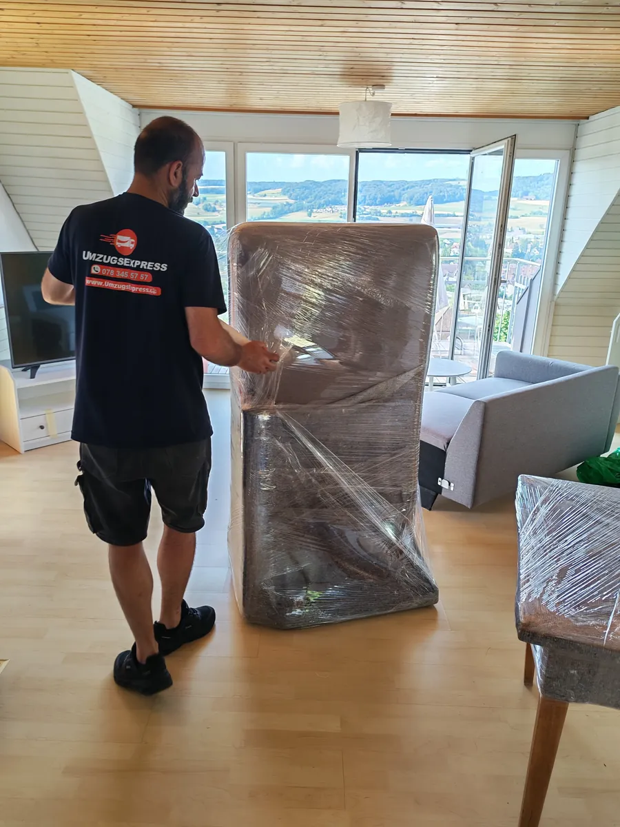 Einsatz von Umzugsexpress: Mitarbeiter bewegt einen in Decken und Folie verpackten Schrank