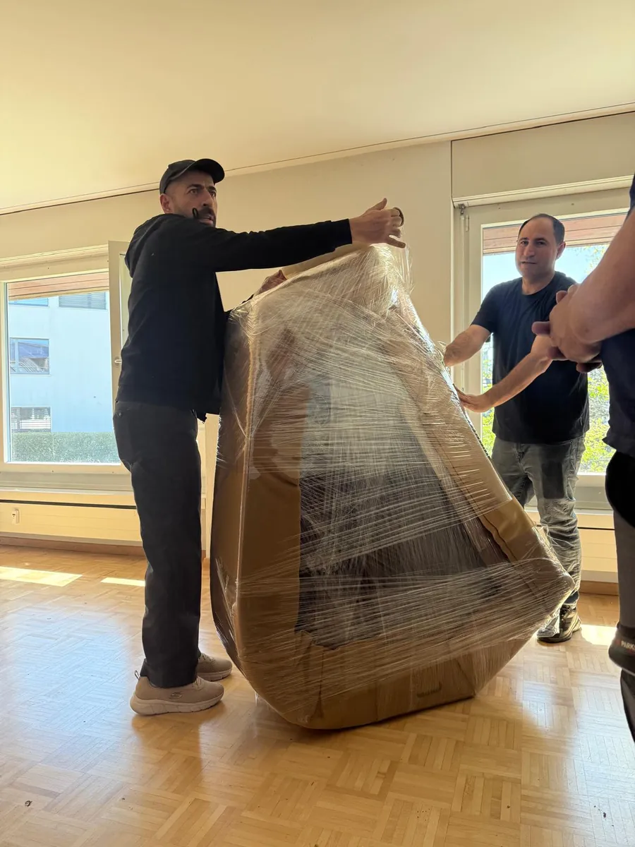 Intervention d’Umzugsexpress : Deux déménageurs emballent un grand fauteuil dans une couverture et du film étirable