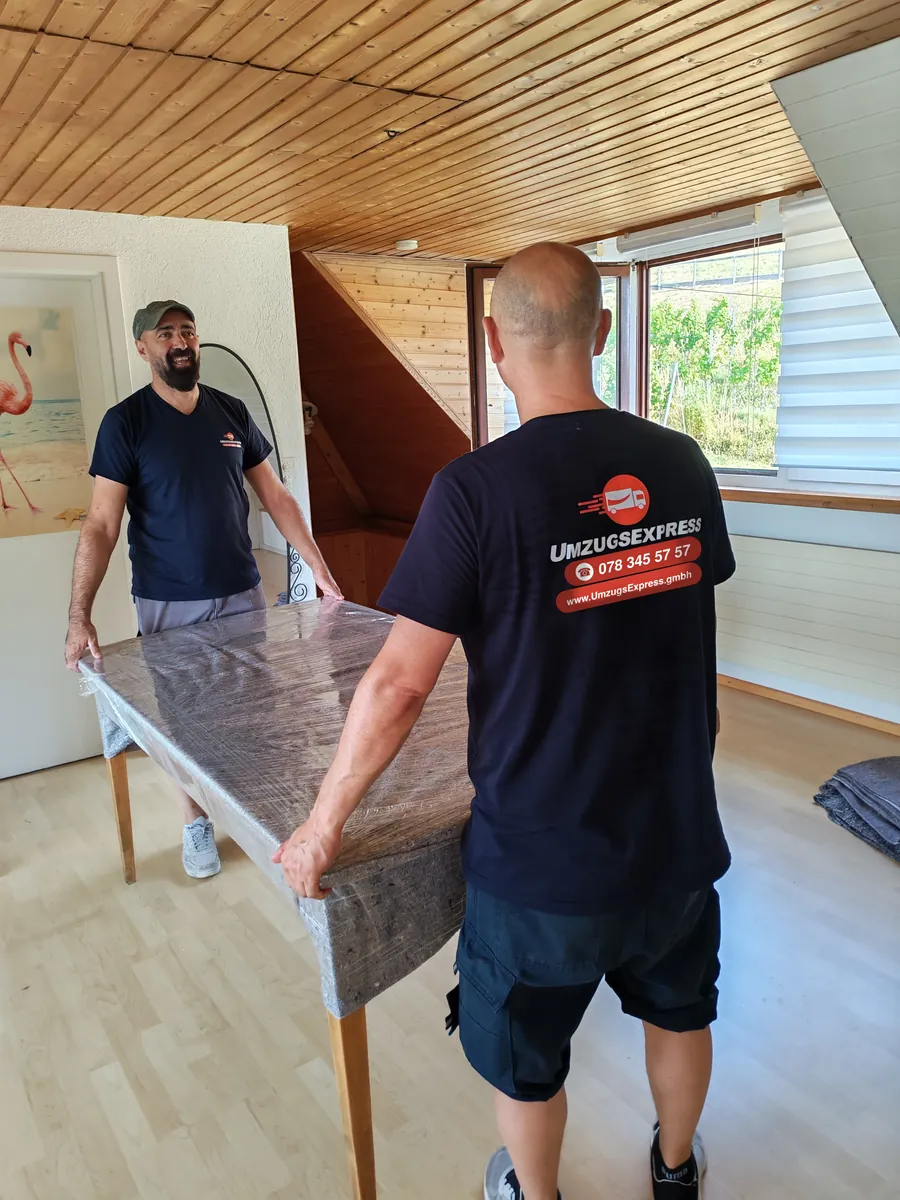 Zwei Mitarbeiter tragen einen verpackten Tisch durch die Wohnung