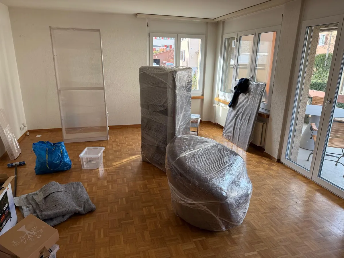 Einsatz von Umzugsexpress: Wohnzimmer mit Schrank und Sessel, in Decken und Folie verpackt, bereit zum Tragen